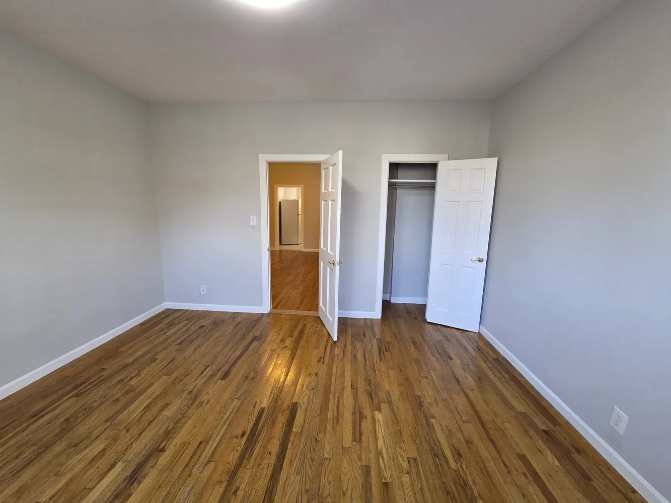 a view of an empty room with wooden floor and closet