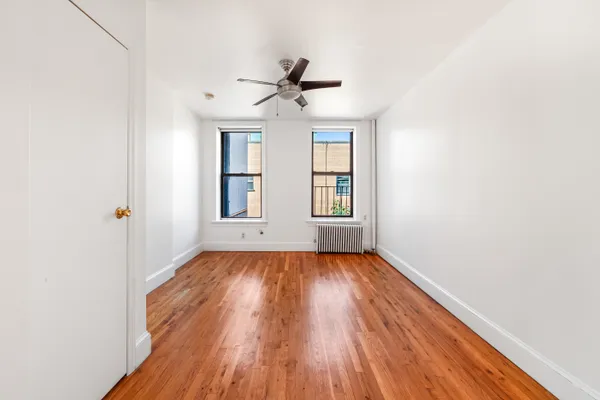 an empty room with wooden floor chandelier fan and windows