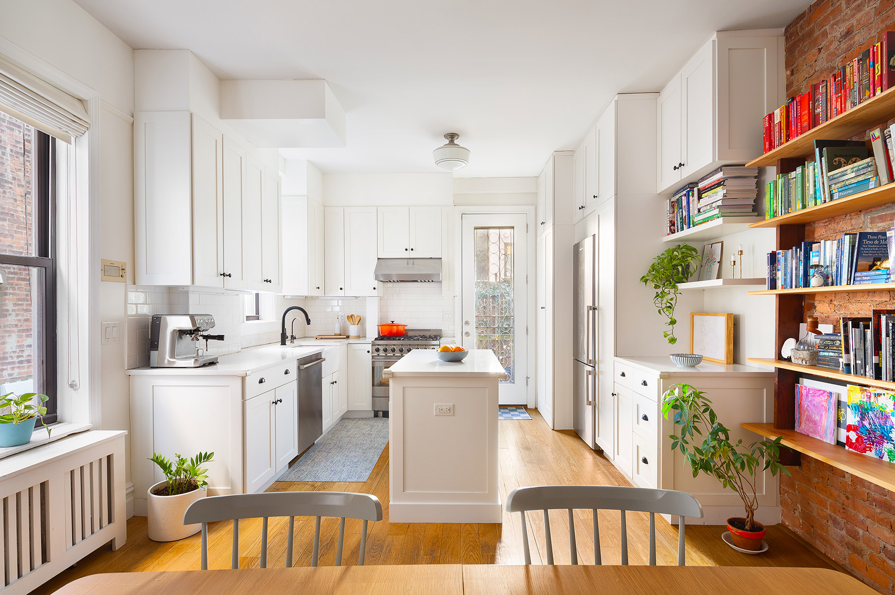 a kitchen with stainless steel appliances lots of white furniture a rug and a book shelf