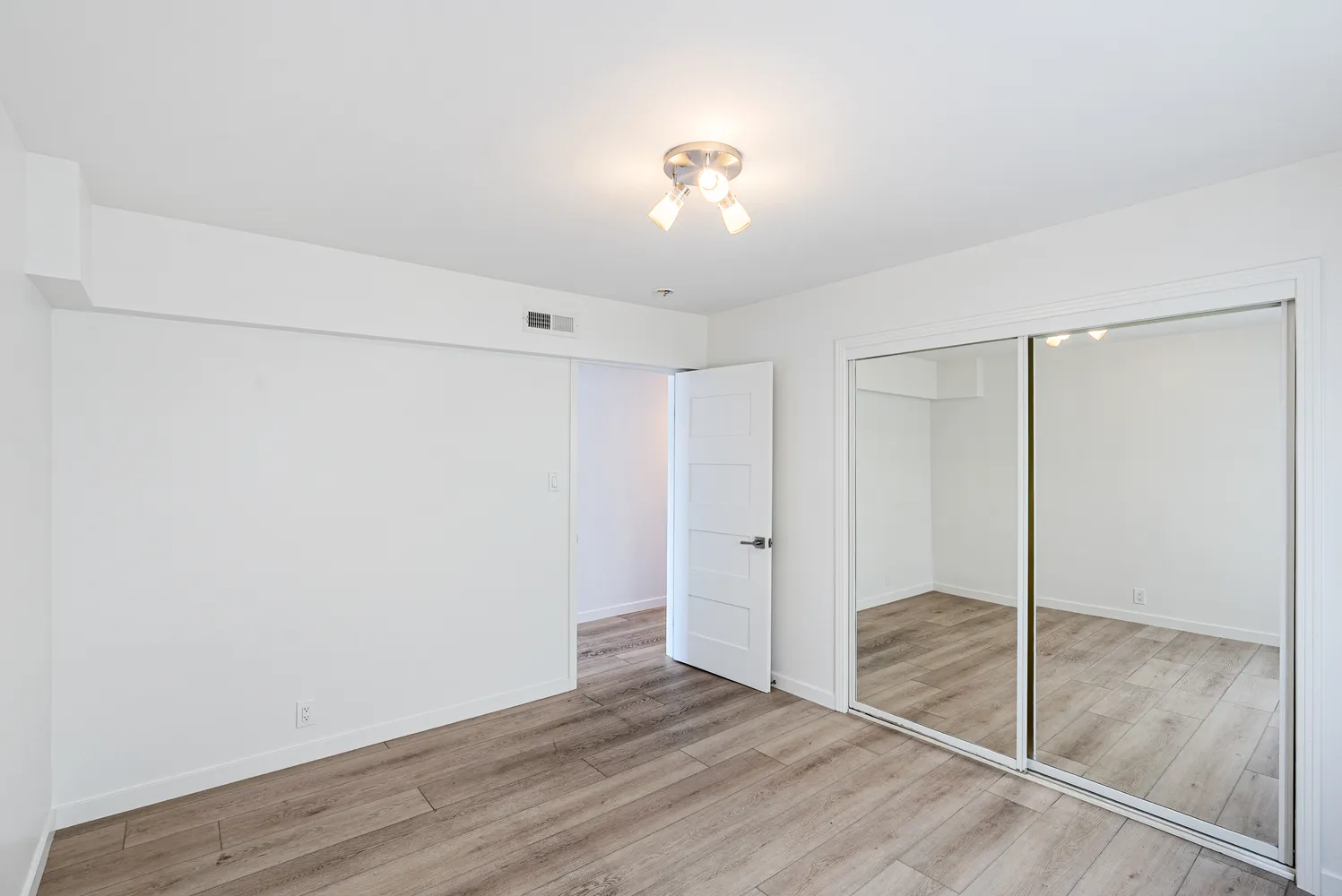 a view of an empty room with wooden floor and a ceiling fan
