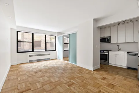 a view of an empty room with window and kitchen view