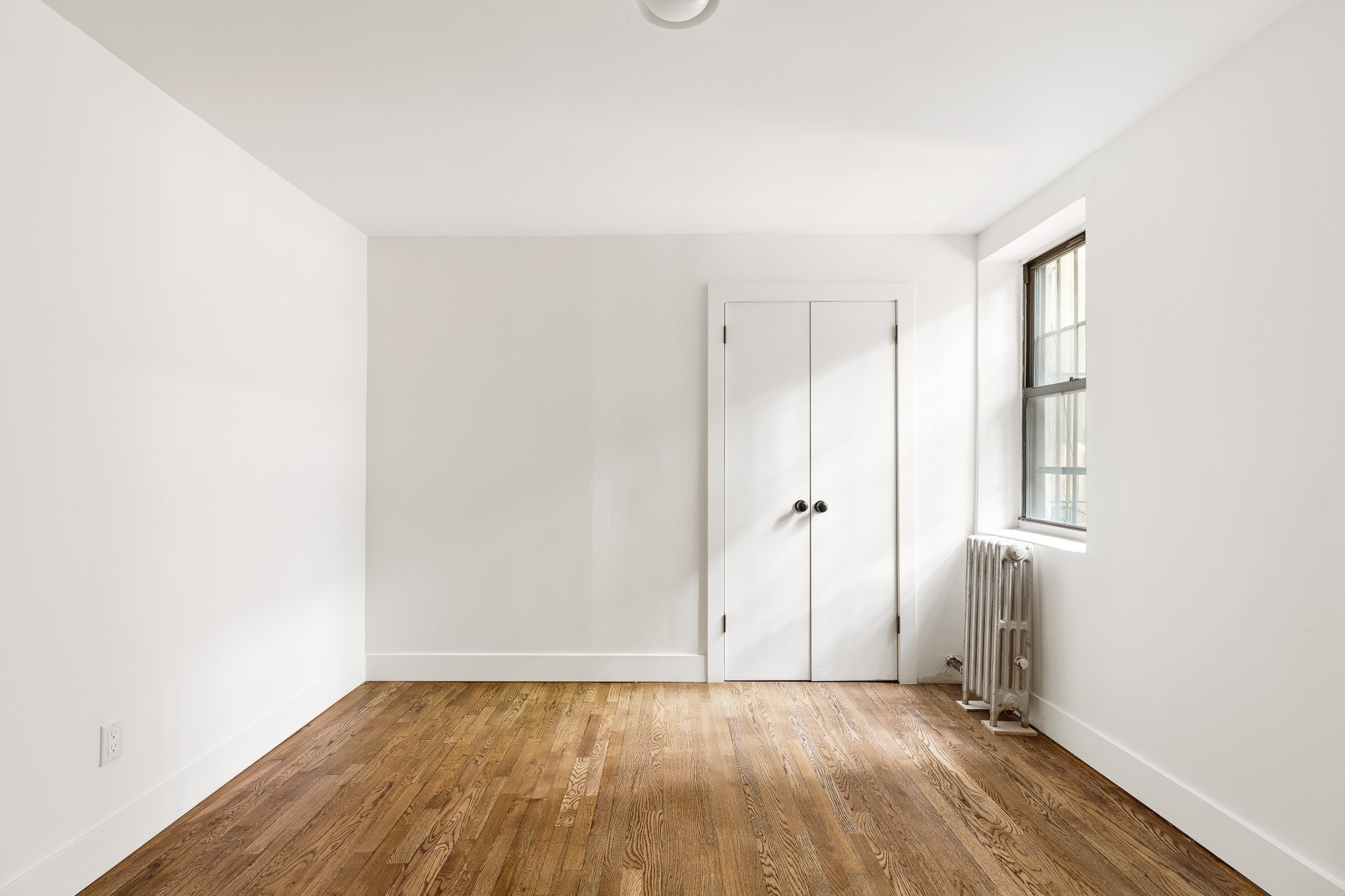 306 Gates Avenue, Unit 1A Brooklyn, NY 11216 - Photo 6 of 14 a view of an empty room with wooden floor and a window