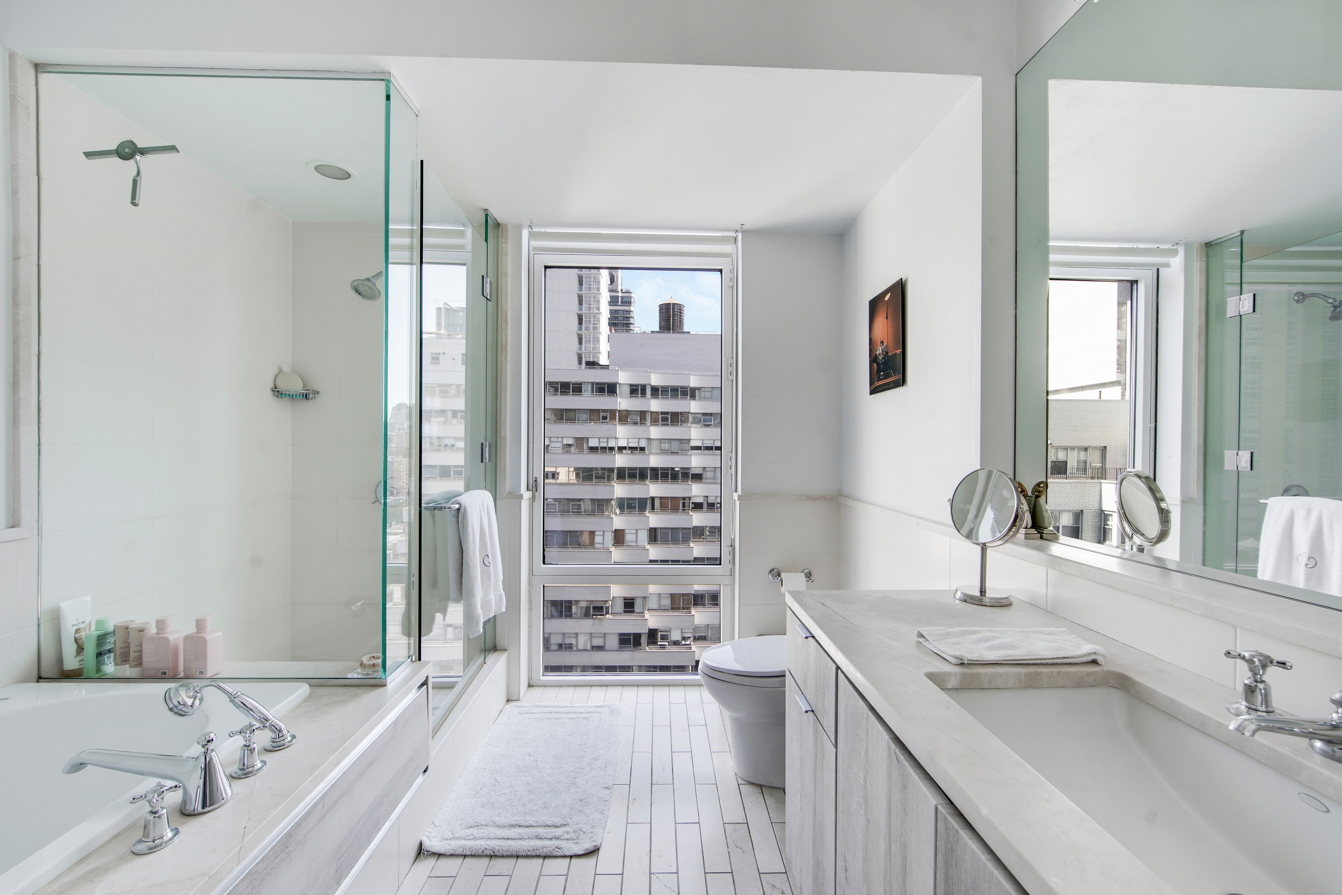 207 East 57th Street, Unit 20A Manhattan, NY 10022 - Photo 17 of 18 a bathroom with a granite countertop double vanity sink a mirror a bathtub and shower