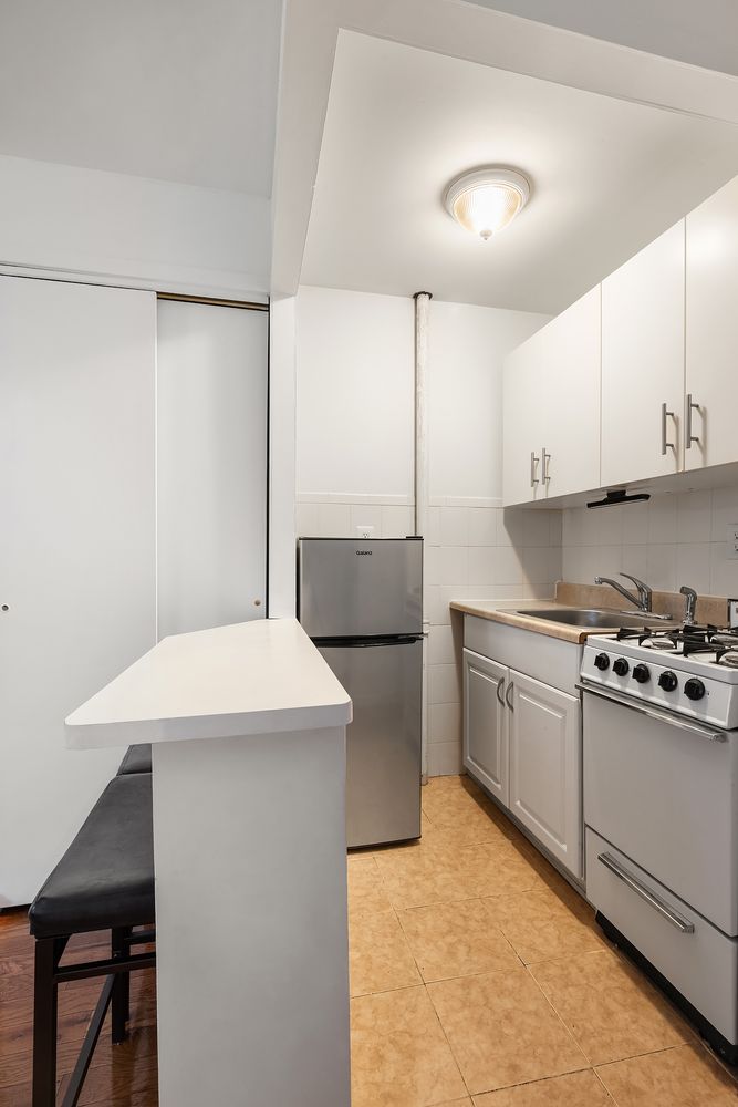 445 West 36th Street Manhattan, NY 10018 - Photo 2 of 11 a kitchen with stainless steel appliances a stove a sink refrigerator and white cabinets with wooden floor