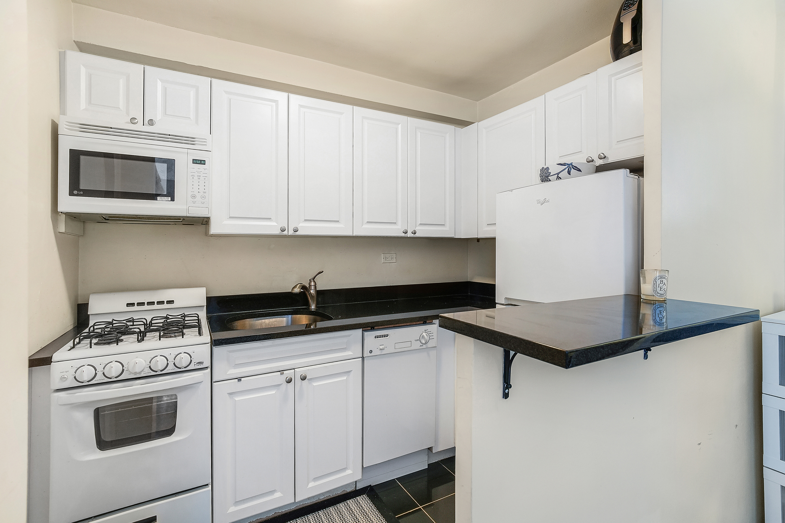 241 East 76th Street, Unit 2G Manhattan, NY 10021 - Photo 3 of 11 a kitchen with granite countertop white cabinets and white appliances