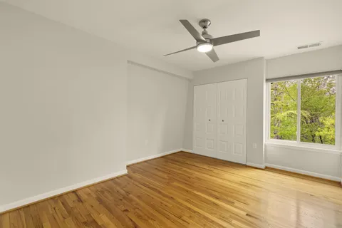 an empty room with wooden floor fan and windows