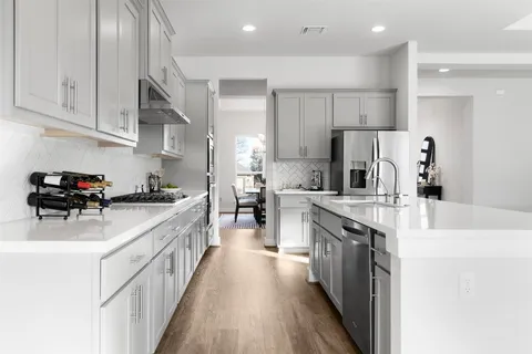 a kitchen with stainless steel appliances a sink dishwasher a stove top oven a refrigerator with white cabinets and wooden floor