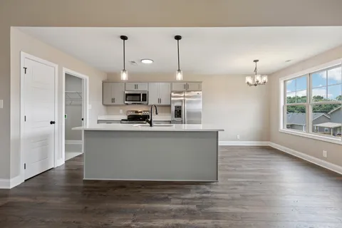 a living room with stainless steel appliances kitchen island granite countertop a stove a sink a refrigerator and white cabinets with wooden floor
