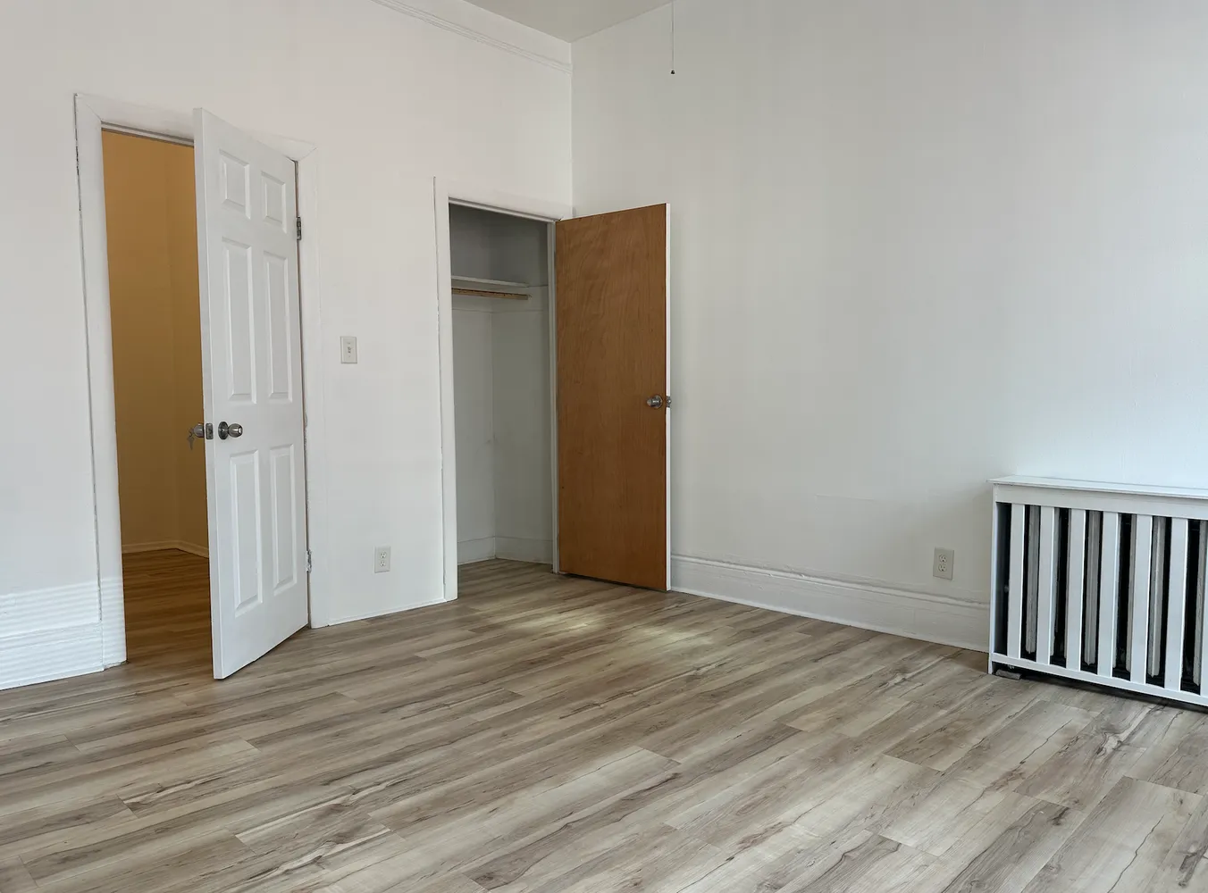 a view of an empty room with wooden floor and closet