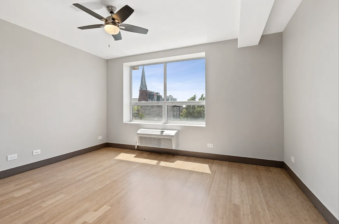 5-43 48th Avenue, Unit 5E Queens, NY 11101 - Photo 3 of 9 an empty room with wooden floor fan and windows