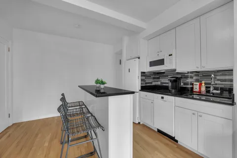 a kitchen with stainless steel appliances a stove a sink a refrigerator white cabinets and wooden floor