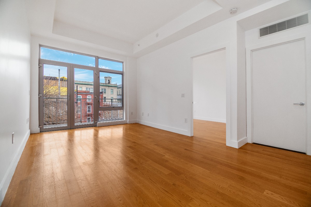a view of an empty room with wooden floor and a window