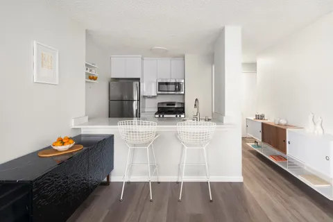 a kitchen with stainless steel appliances kitchen island granite countertop a stove a sink a refrigerator and white cabinets with wooden floor