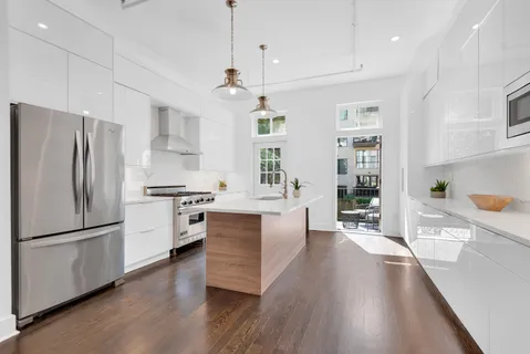 a kitchen with stainless steel appliances a refrigerator a sink dishwasher a oven a dining table and chairs with wooden floor