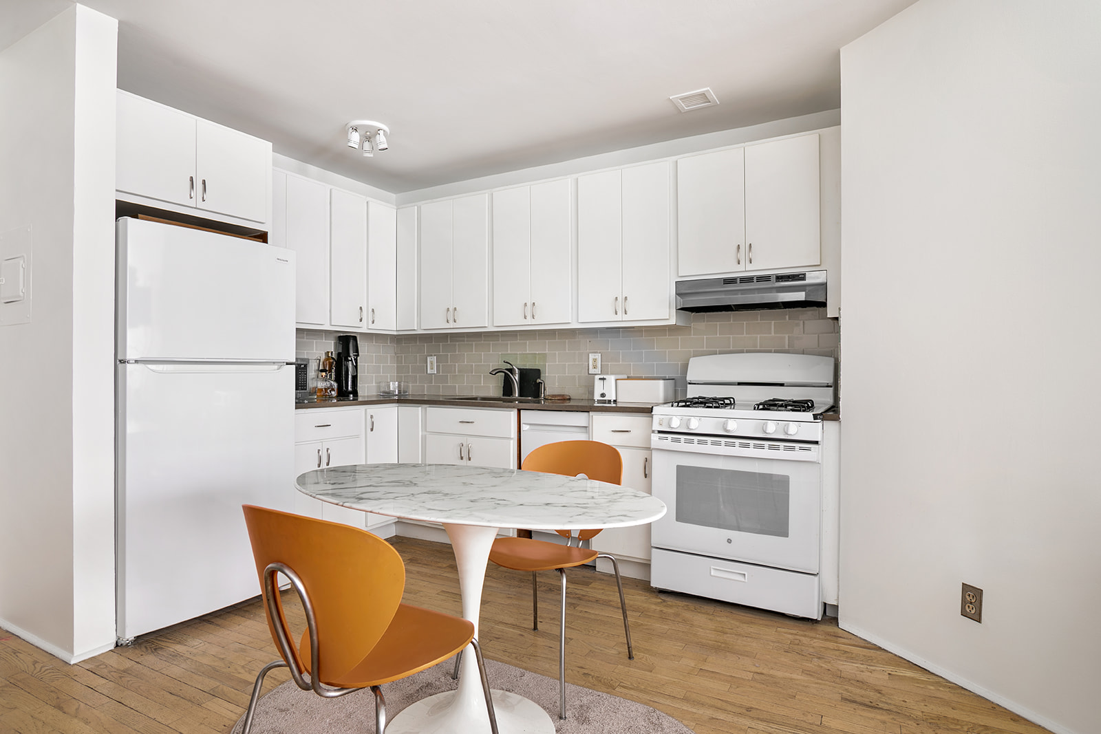 167 Perry Street, Unit 5K Manhattan, NY 10014 - Photo 4 of 10 a kitchen with stainless steel appliances granite countertop a stove a refrigerator a sink a dining table and chairs with wooden floor