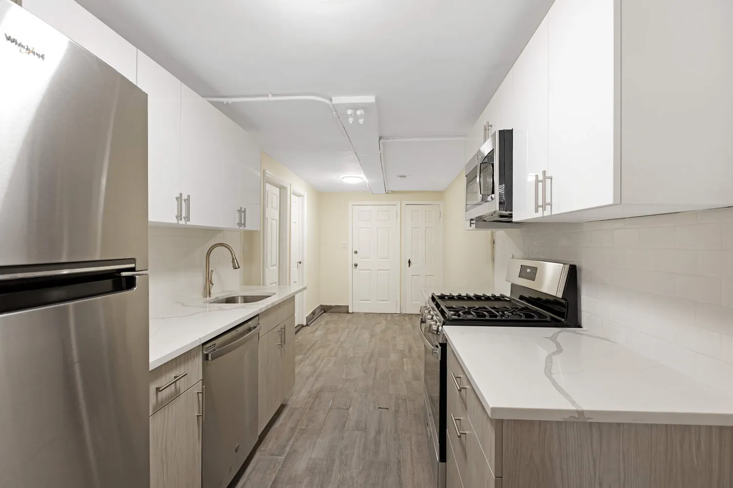 a kitchen with stainless steel appliances a sink dishwasher a refrigerator a microwave oven and white cabinets with wooden floor