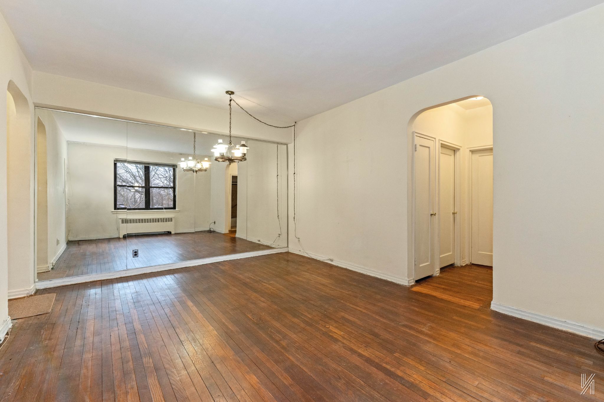 22-60 79th Street, Unit 1A Queens, NY 11370 - Photo 4 of 17 an empty room with wooden floor and mirror