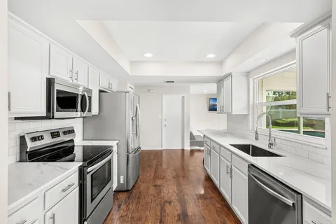 a kitchen with stainless steel appliances a sink dishwasher a stove top oven a refrigerator with wooden floor and cabinets