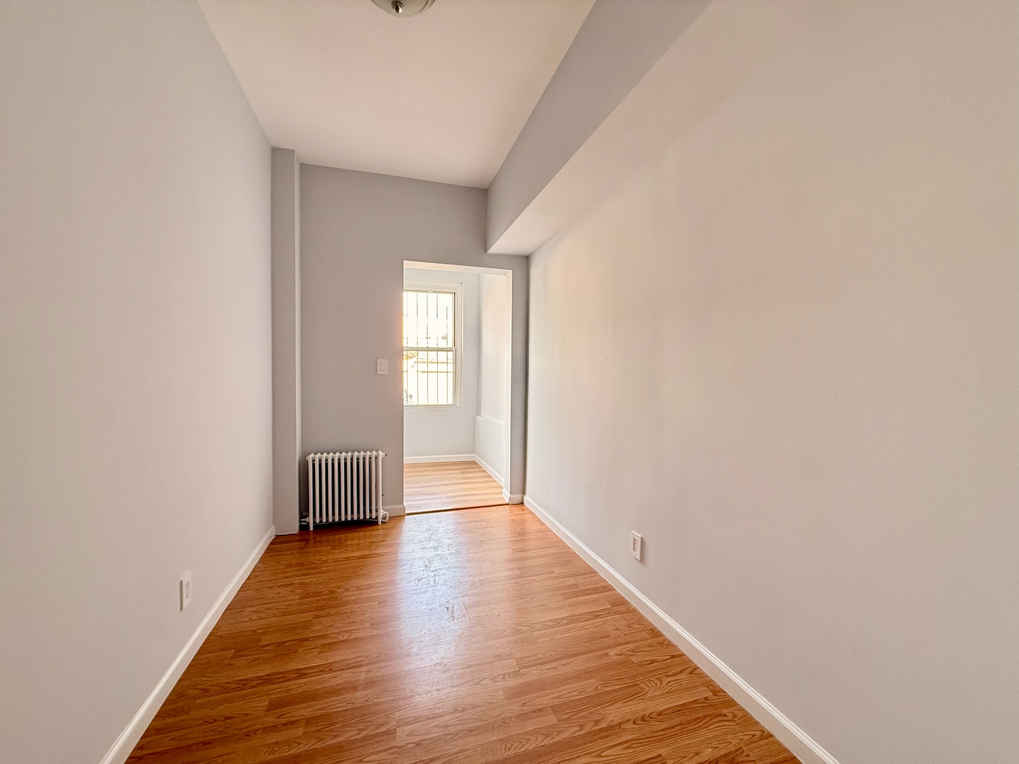 1675 85th Street, Unit 1R Brooklyn, NY 11214 - Photo 4 of 8 a view of an empty room with wooden floor and a window