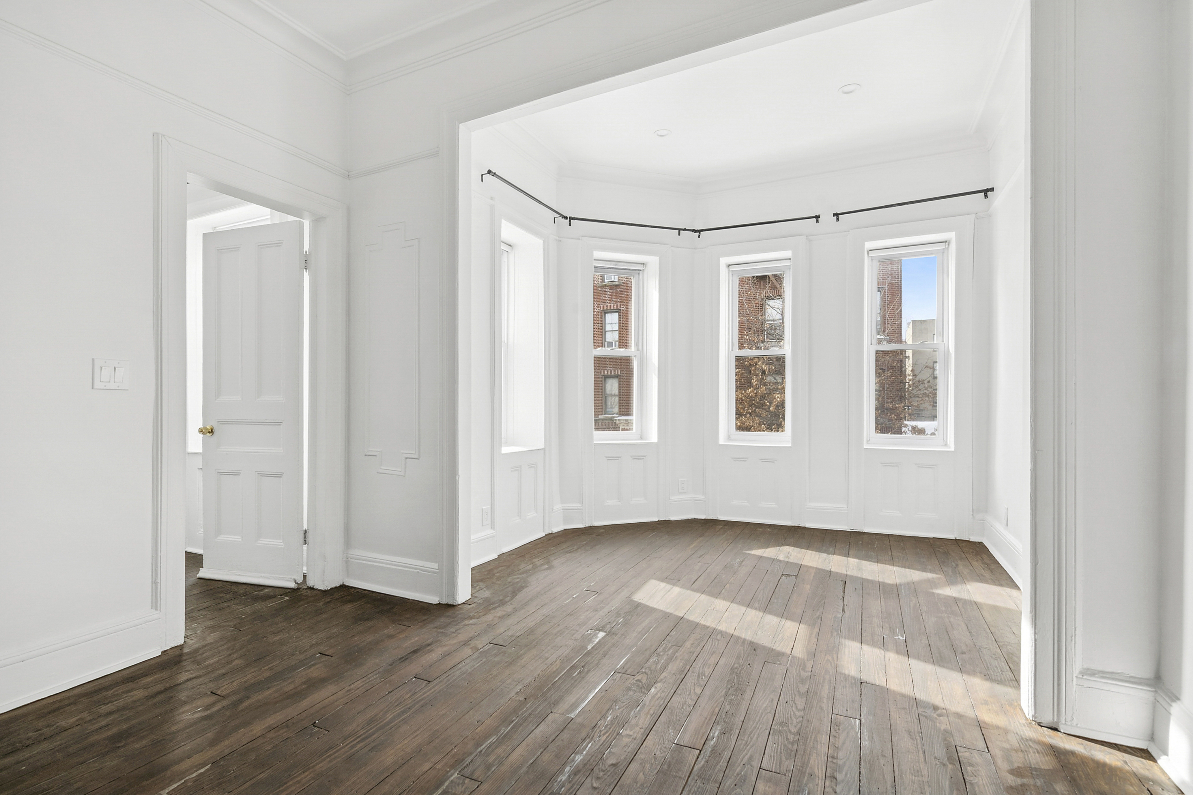 a view of an empty room with wooden floor and windows