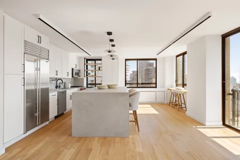 a living room with stainless steel appliances kitchen island granite countertop a refrigerator a stove and a wooden floors