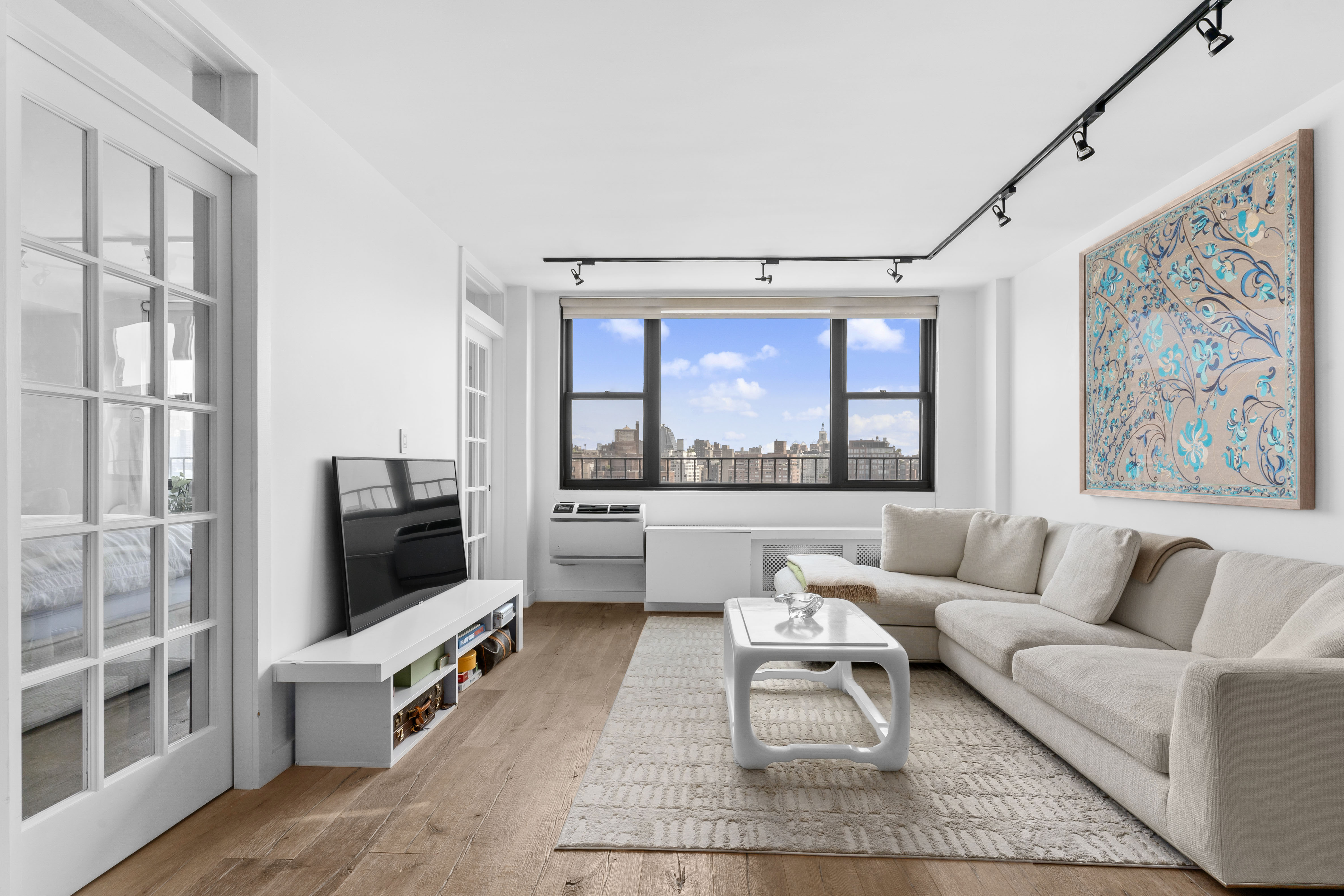 61 Jane Street, Unit 19E Manhattan, NY 10014 - Photo 1 of 9 a living room with furniture a flat screen tv and a floor to ceiling window