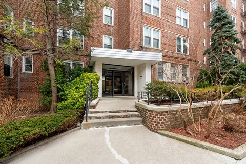 a view of a brick house with plants and large tree