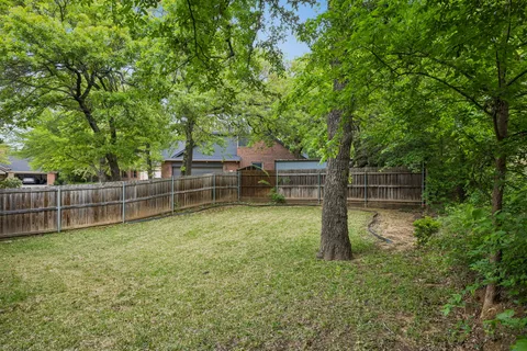 a backyard of a house with large trees and wooden fence