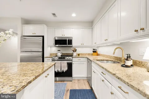 a kitchen with granite countertop a sink stainless steel appliances and white cabinets