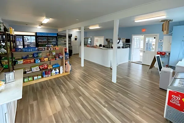 an empty room with wooden floor and way to kitchen