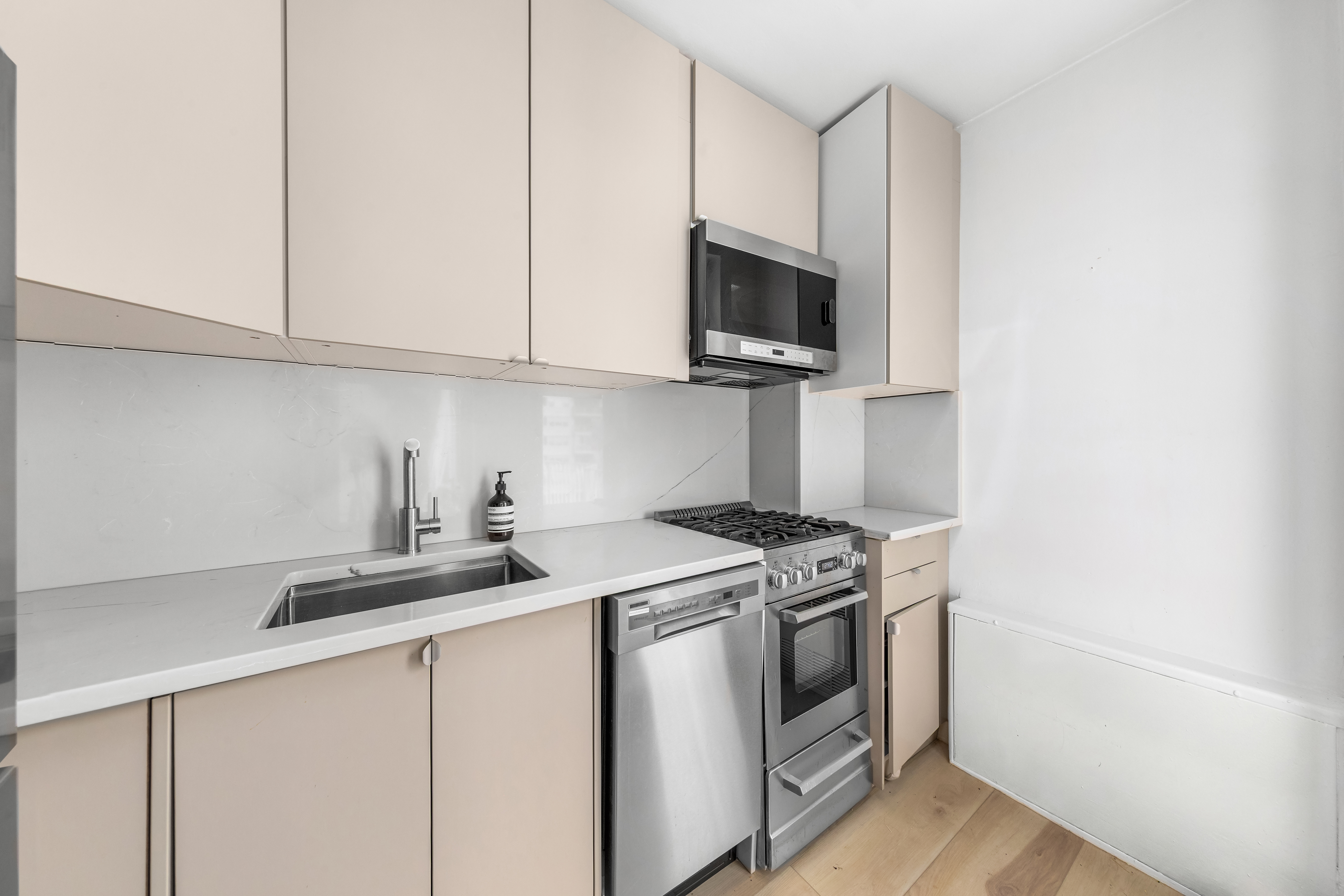 1160 3rd Avenue, Unit 12C Manhattan, NY 10065 - Photo 4 of 6 a kitchen with stainless steel appliances granite countertop white cabinets a sink a stove and a microwave