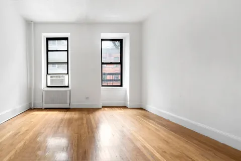 an empty room with wooden floor closet and windows