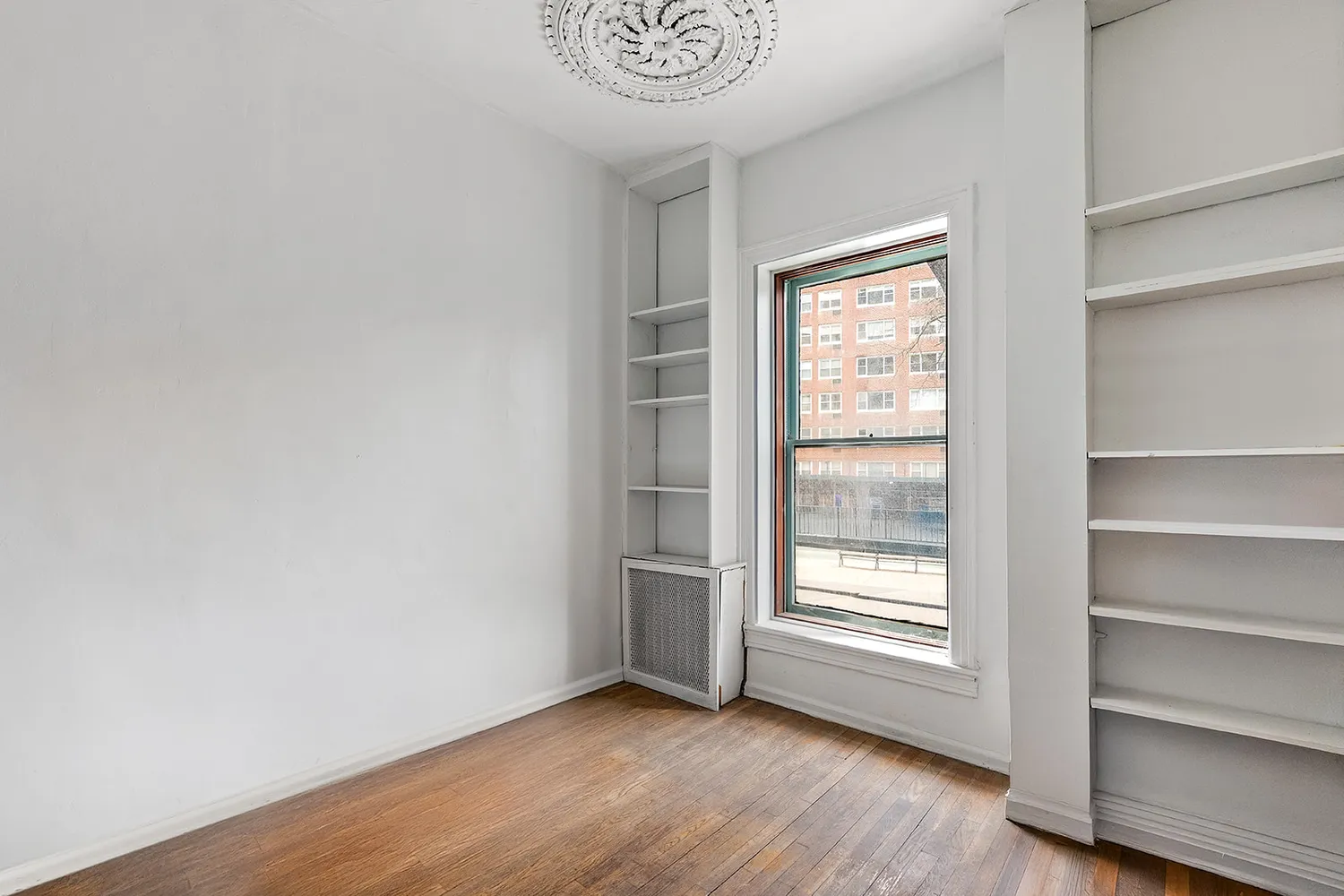 a view of an empty room with a window and wooden floor