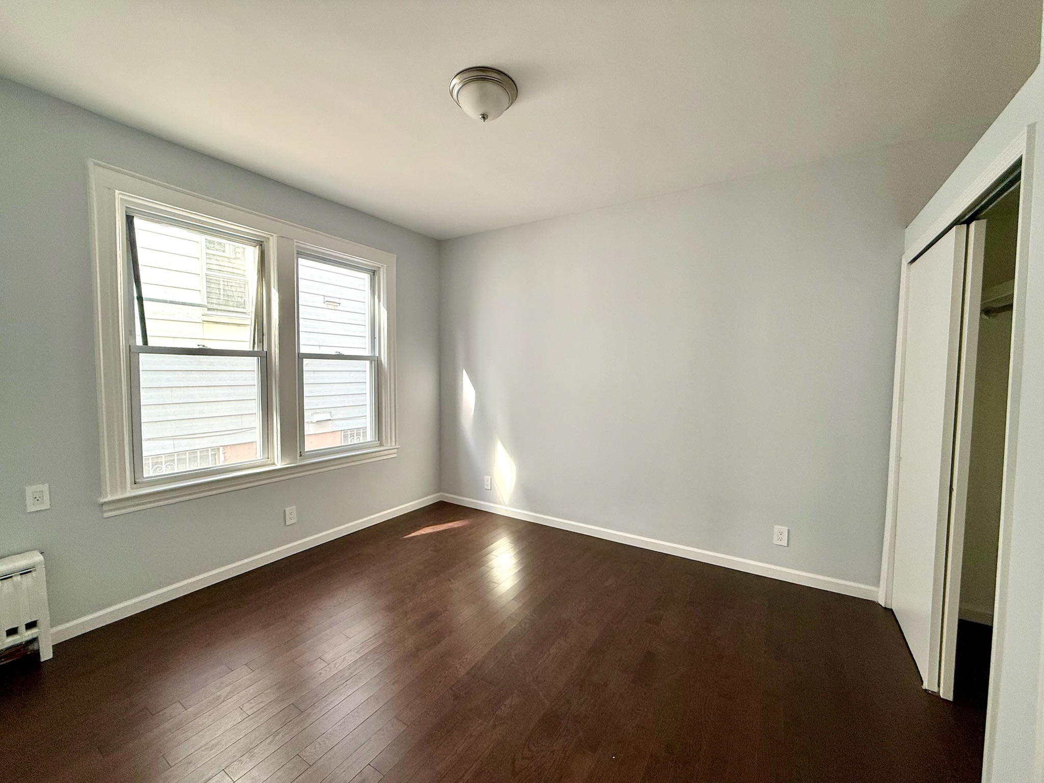 1675 85th Street, Unit 1F Brooklyn, NY 11214 - Photo 5 of 7 an empty room with wooden floor and windows with curtains