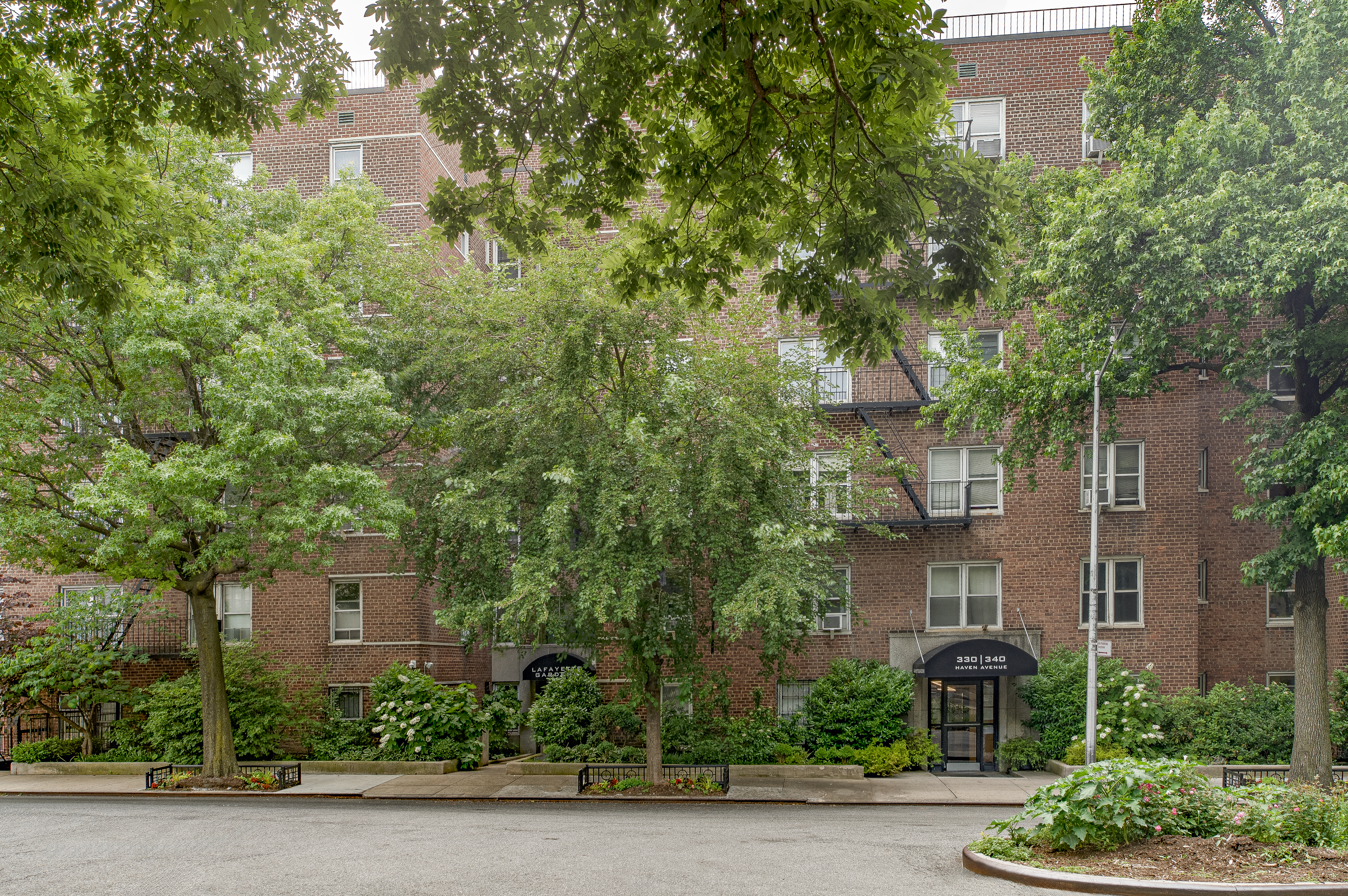 340 Haven Avenue, Unit 2H Manhattan, NY 10033 - Photo 21 of 24 a view of a tall brick building next to a road with large trees