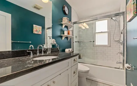 a bathroom with a granite countertop sink a toilet a mirror and shower