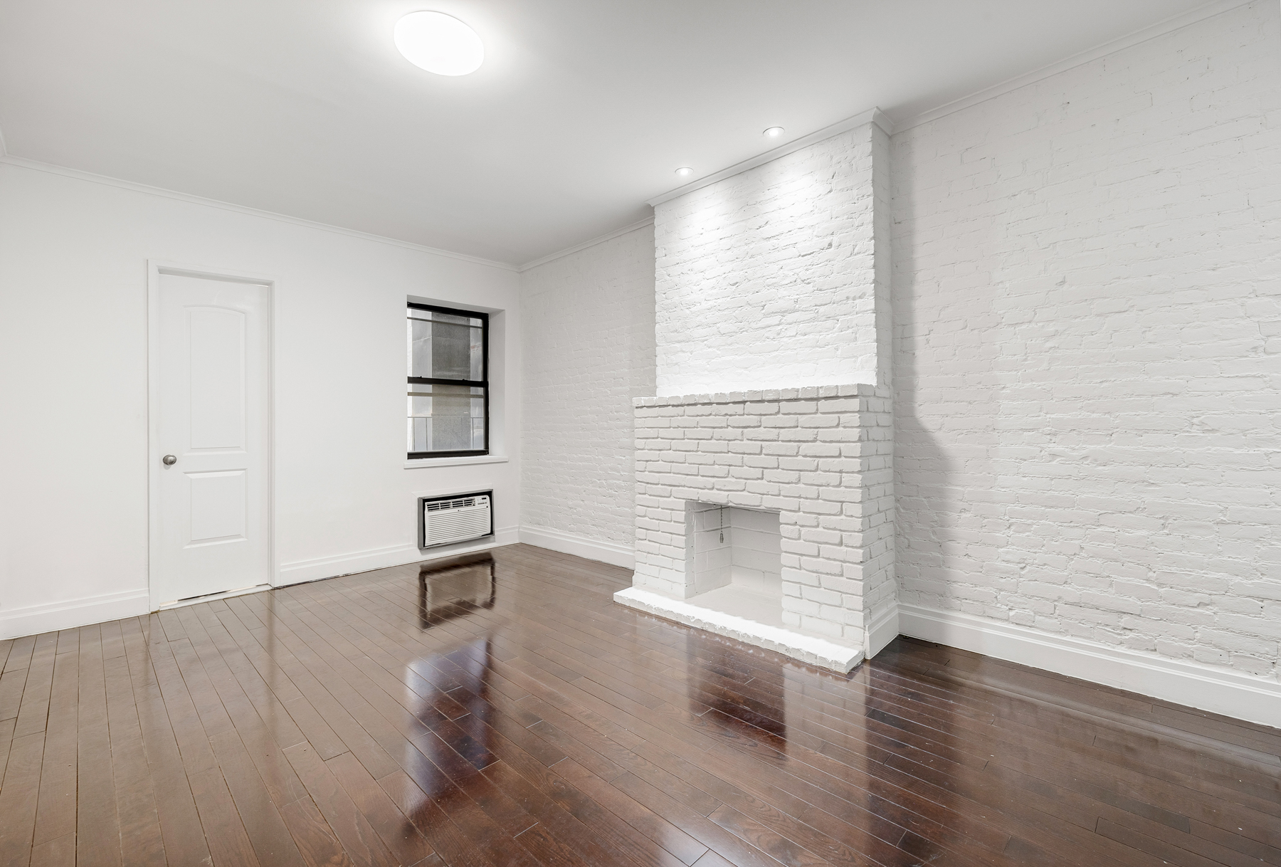 an empty room with wooden floor fireplace and windows