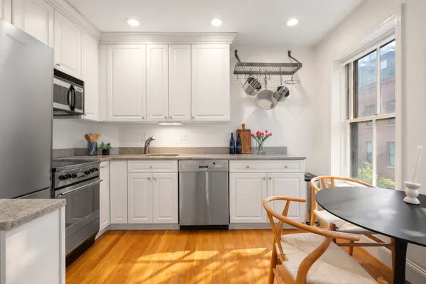 a kitchen with stainless steel appliances granite countertop a stove top oven a sink dishwasher and white cabinets with wooden floor