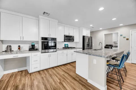a kitchen with stainless steel appliances granite countertop a stove a sink a microwave a refrigerator and white cabinets with wooden floor