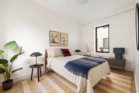 a bedroom with a bed a couch and potted plant on the dresser