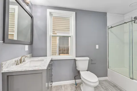 a bathroom with a granite countertop toilet a sink a mirror and a window
