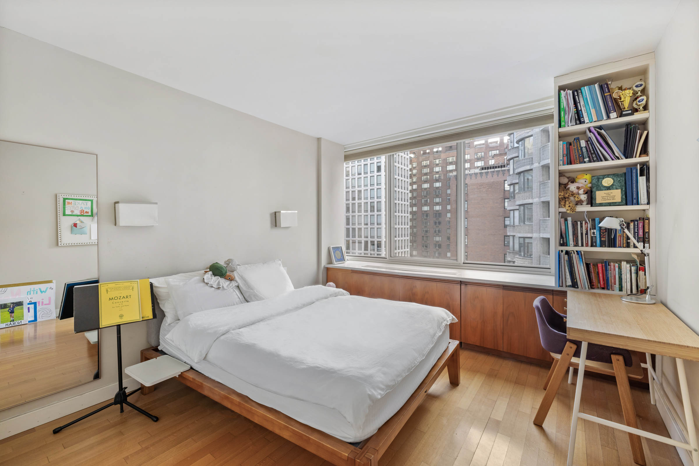 61 West 62nd Street, Unit 23G Manhattan, NY 10023 - Photo 6 of 9 a bedroom with a bed and a bookshelf with wooden floor