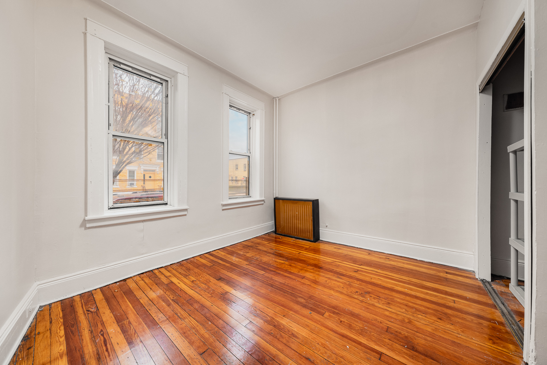 70-03 66th Street, Unit 1L Queens, NY 11385 - Photo 7 of 8 a view of an empty room with wooden floor and a window