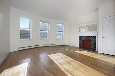 an empty room with wooden floor fireplace and windows