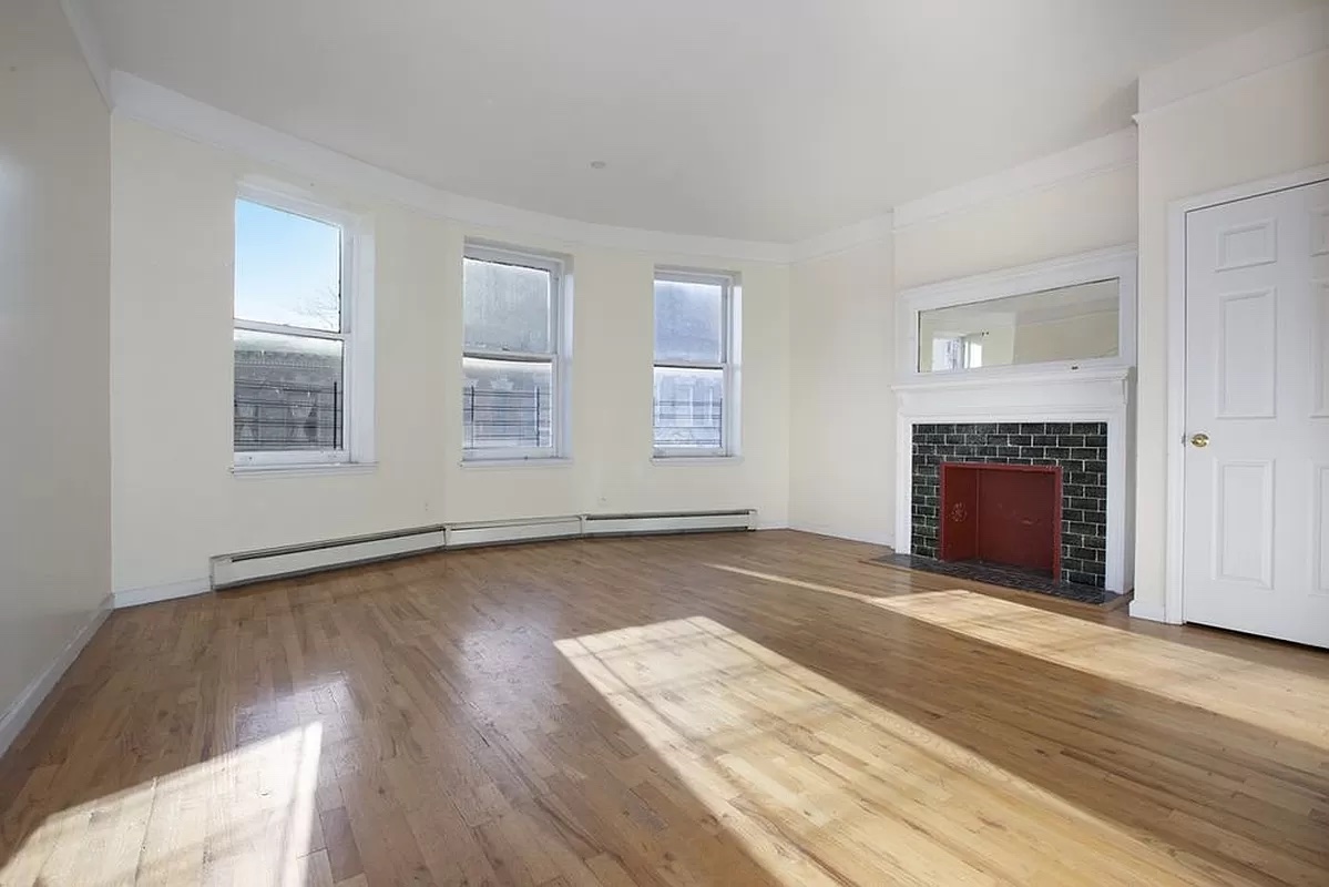 469 West 141st Street Manhattan, NY 10031 - Photo 9 of 14 an empty room with wooden floor fireplace and windows