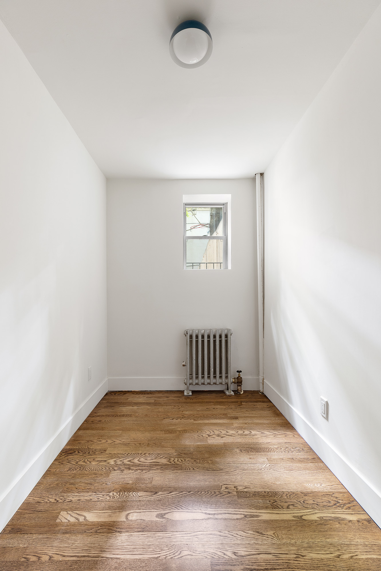 306 Gates Avenue, Unit 1A Brooklyn, NY 11216 - Photo 7 of 14 an empty room with a exposed radiator and wooden floor