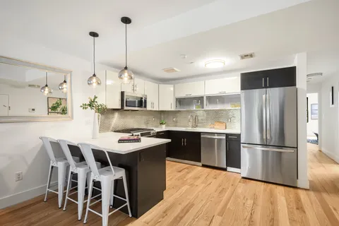 a kitchen with stainless steel appliances kitchen island granite countertop a sink a stove a refrigerator and island with wooden floor