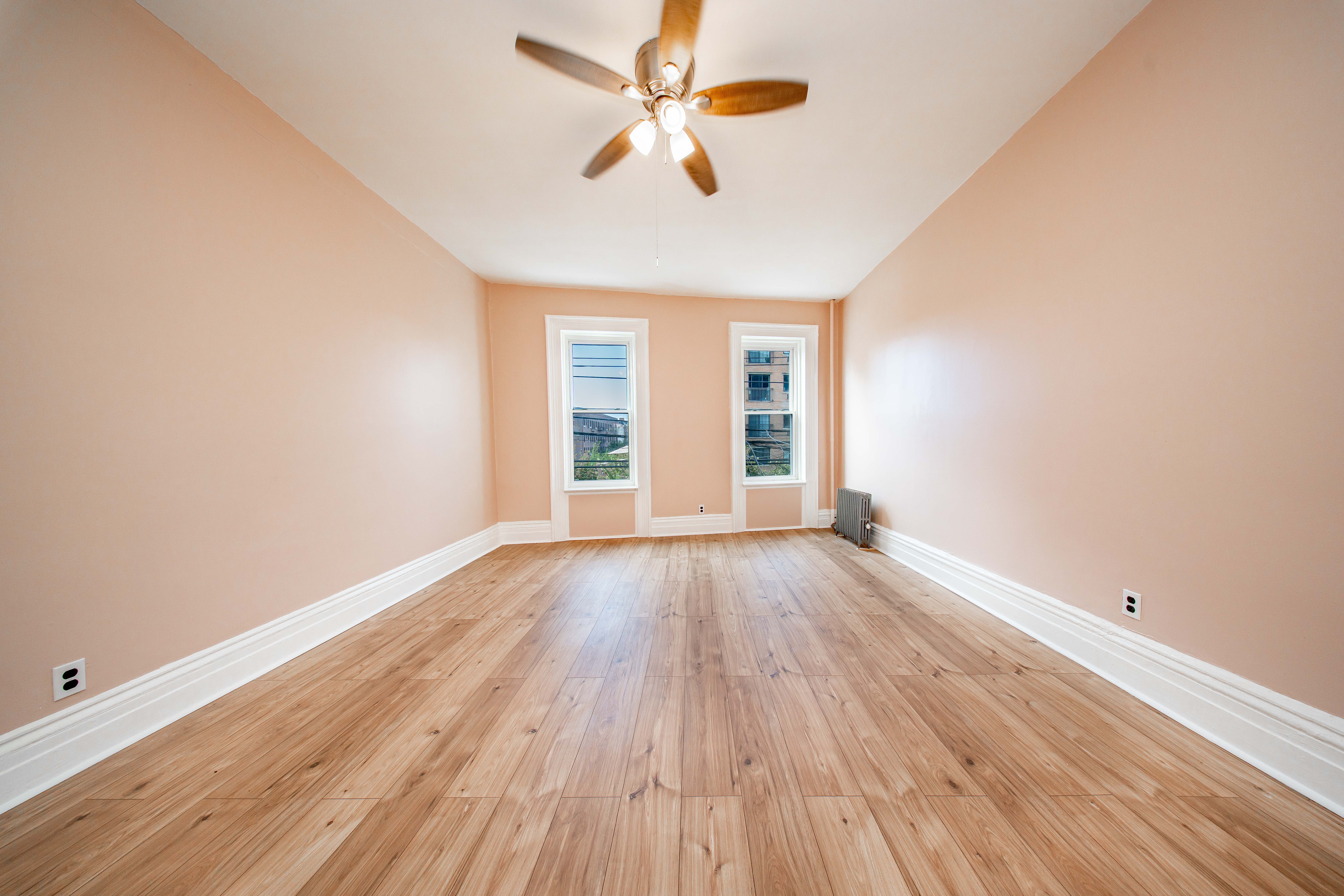 22-17 Astoria Boulevard, Unit 2W Queens, NY 11102 - Photo 2 of 10 an empty room with wooden floor chandelier fan and windows