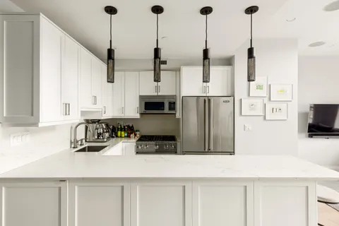 a kitchen with stainless steel appliances kitchen island granite countertop a refrigerator a oven and white cabinets