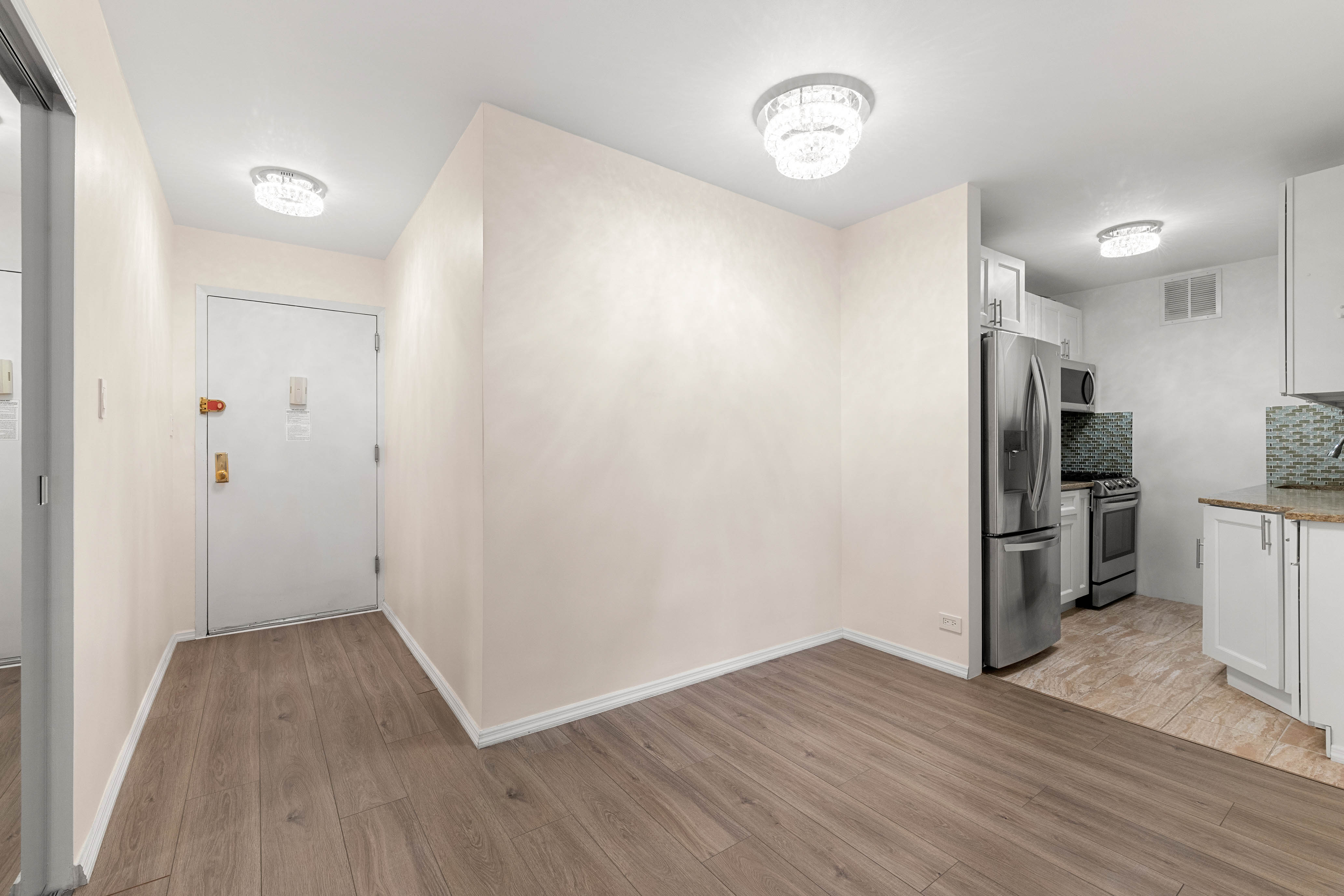 102-10 66th Road, Unit 21K Queens, NY 11375 - Photo 4 of 16 an empty room with wooden floor and a kitchen